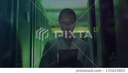 Monitoring data on tablet, technician in lab coat navigating server aisle, cables and LED lights Monitoring data on tablet, technician in lab coat navigating server aisle, cables and LED lights 135824803