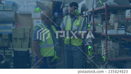 Two warehouse workers wearing high-visibility vests reviewing stock in warehouse, with clipboard 135824823