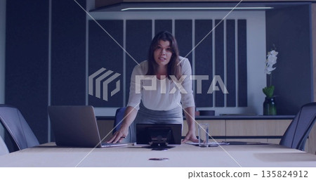 Leaning businesswoman addressing conference attendees, with laptop speakerphone documents and water Leaning businesswoman addressing conference attendees, with laptop speakerphone documents and water 135824912