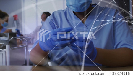Technician wearing blue scrubs mask and gloves handling test device in production lab, with overlay 135824916