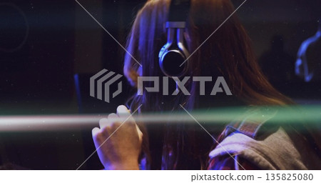 Singing recording artist wearing headphones and holding condenser mic in booth, light streaks 135825080
