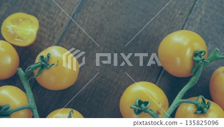 Displaying yellow cherry tomatoes on wooden kitchen tabletop, with green vines, halved tomato Displaying yellow cherry tomatoes on wooden kitchen tabletop, with green vines, halved tomato 135825096