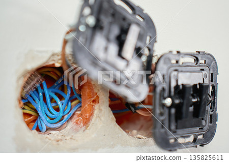 Electrical light switch with exposed wiring and mounting boxes inside white wall. Process of installing electrical sockets. Concept of electrical installation, repair, maintenance and home renovation 135825611