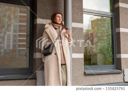 white Caucasian woman drinks coffee on street near the entrance to building. Coffee break white Caucasian woman drinks coffee on street near the entrance to building. Coffee break 135825791