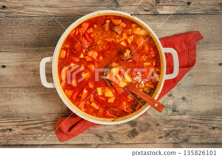 Cooking stew with vegetables and meat in a large pot on wooden table with red cloth Cooking stew with vegetables and meat in a large pot on wooden table with red cloth 135826101
