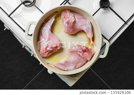 Raw rabbit legs are browned in a frying pan with melted butter and olive oil 135826106
