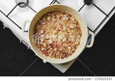 Cooking a dish with onions, meat, and spices on a white stove in the kitchen Cooking a dish with onions, meat, and spices on a white stove in the kitchen 135826107