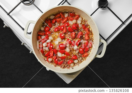 Cooking with tomatoes and onions on a stove in a kitchen setting during the afternoon 135826108