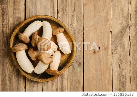 Fresh king oyster mushrooms arranged in a wooden bowl on a rustic wooden table surface Fresh king oyster mushrooms arranged in a wooden bowl on a rustic wooden table surface 135826132