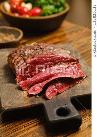 Sliced beef resting on wooden board with seasoning and fresh vegetables nearby Sliced beef resting on wooden board with seasoning and fresh vegetables nearby 135826133