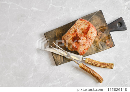 Cooking meat on a cutting board with knife and fork in a kitchen setting Cooking meat on a cutting board with knife and fork in a kitchen setting 135826148