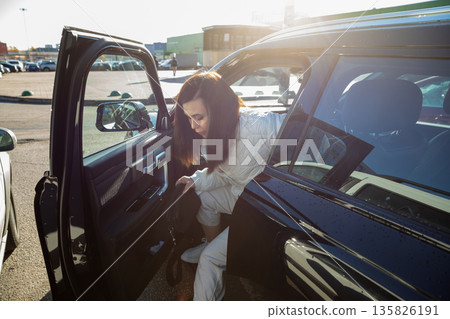 Woman getting out of her car in a parking lot. Daily commute or travel for adult or youth. Automobile ownership concept. Woman getting out of her car in a parking lot. Daily commute or travel for adult or youth. Automobile ownership concept. 135826191