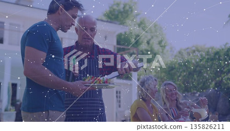 Grilling senior wearing apron transferring skewers at backyard barbecue, with spatula and pitcher Grilling senior wearing apron transferring skewers at backyard barbecue, with spatula and pitcher 135826211