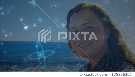 Smiling woman wearing dark shirt standing by seaside, with glowing molecular holograms, copy space Smiling woman wearing dark shirt standing by seaside, with glowing molecular holograms, copy space 135826305