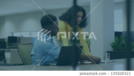 Pointing colleagues in business attire reviewing documents at desk with laptop and water glasses 135826321