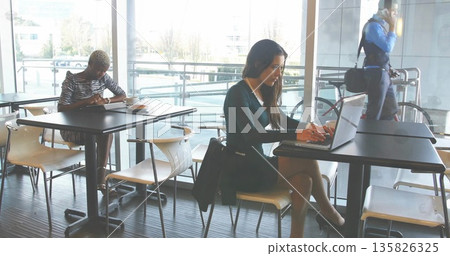 Typing businesswoman wearing dark dress working on laptop in lounge, with terrace view and bicycle 135826325