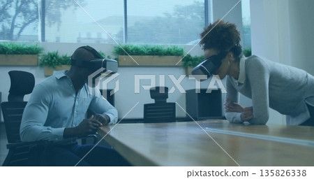 Office colleagues wearing VR headsets leaning over wooden table in meeting room, with planter boxes Office colleagues wearing VR headsets leaning over wooden table in meeting room, with planter boxes 135826338
