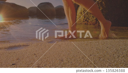 Stepping barefoot man wearing trunks into shallow water on beach, rounded boulders, rock formation Stepping barefoot man wearing trunks into shallow water on beach, rounded boulders, rock formation 135826388
