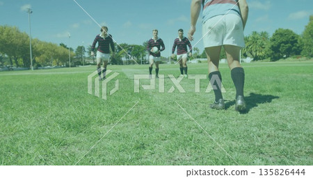 Walking rugby teammates approaching player from midfield line on grass field, with rugby ball 135826444