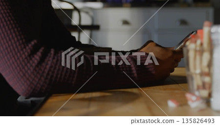 Sitting man wearing burgundy sweater holding smartphone at cafe table, stirrer jar and condiments Sitting man wearing burgundy sweater holding smartphone at cafe table, stirrer jar and condiments 135826493