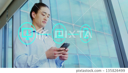 Holding smartphone Asian professional displaying teal network icons in office tower window Holding smartphone Asian professional displaying teal network icons in office tower window 135826499