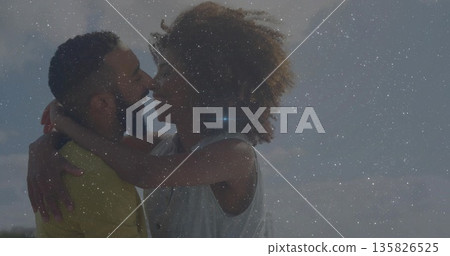 Smiling couple wearing casual tops hugging under bright sky with particle overlay Smiling couple wearing casual tops hugging under bright sky with particle overlay 135826525