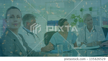 Medical and administrative team in scrubs and suits reviewing charts at table in hospital boardroom 135826529