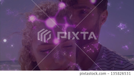 Standing couple embracing on beach, with swimsuit and striped tshirt under glowing purple patterns 135826531