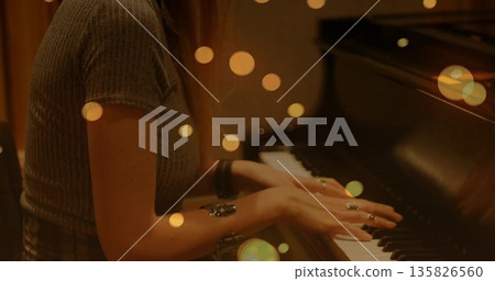 Pianist wearing ribbed top and rings playing piano keys in music room, with amber bokeh lights Pianist wearing ribbed top and rings playing piano keys in music room, with amber bokeh lights 135826560
