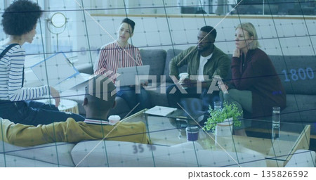 Collaborating colleagues sitting around glass-top table in office lounge, with binder and laptops Collaborating colleagues sitting around glass-top table in office lounge, with binder and laptops 135826592