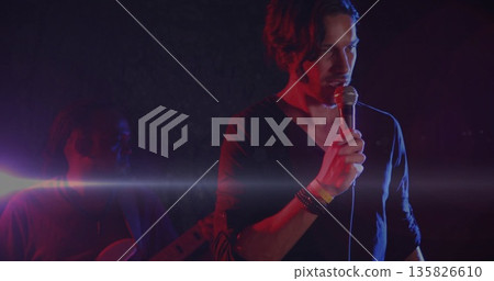 Gripping wired mic vocalist and bassist playing bass wearing bracelets onstage with colored lights 135826610
