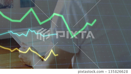 Reviewing papers man in button-up shirt at office desk, with grid and colored line graphs 135826628
