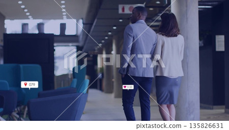 Walking business couple wearing grey and white blazers down office corridor, with lounge chairs 135826631