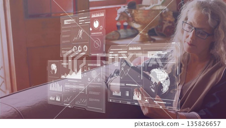 Woman wearing cardigan holding tablet with holographic graphs on sofa at home, copy space Woman wearing cardigan holding tablet with holographic graphs on sofa at home, copy space 135826657