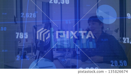 Female office worker talking on smartphone at office desk, with monitor and digital charts Female office worker talking on smartphone at office desk, with monitor and digital charts 135826674