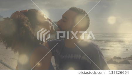 Leaning couple embracing at seaside boardwalk during sunset, metal railing casting warm glow 135826694