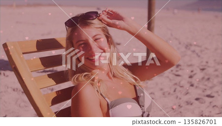 Woman wearing bikini adjusting sunglasses on beach chair at seaside with pink hearts, copy space 135826701