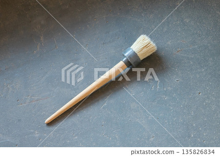 hand held paint brush designed for priming and painting surfaces. Round paint brush with wooden handle for priming and painting work on gray textured surface. Tool for home renovation and maintenance 135826834