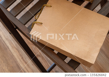 Kraft paper bag. Brown paper shopping bag mockup with rope handle on wooden chair. Retail packaging design template for boutique, gift or sale promotion. purchase, gift, sale Kraft paper bag. Brown paper shopping bag mockup with rope handle on wooden chair. Retail packaging design template for boutique, gift or sale promotion. purchase, gift, sale 135826842