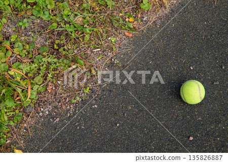 Tennis ball on asphalt ground next to green grass and dirt. Sport equipment outdoors for game or practice. Playing with a dog. Top view Tennis ball on asphalt ground next to green grass and dirt. Sport equipment outdoors for game or practice. Playing with a dog. Top view 135826887