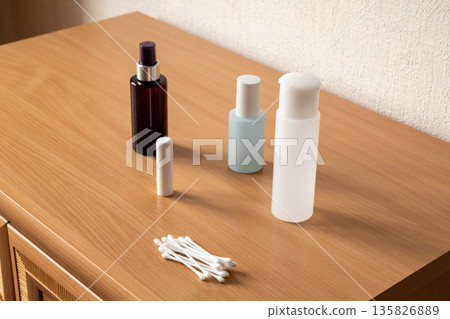Cosmetic bottles and cotton swab on wooden table for beauty product advertisement. Minimalist essential personal care items. Cosmetic bottles and cotton swab on wooden table for beauty product advertisement. Minimalist essential personal care items. 135826889