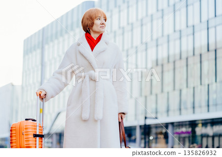 Smiling independent woman with suitcase using smartphone in modern city Female traveler with luggage, urban commute, independent lifestyle, city transportation, daily routine. 135826932