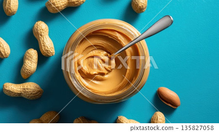 Peanut butter jar with a spoon sits surrounded by peanuts on a blue background 135827058