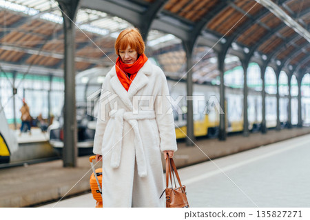 Redhead Caucasian middle age woman in white coat walking slowly on railway platform with suitcase, looking down, emotional pause, solitude, inner balance, life pressure, mental wellbeing moment Redhead Caucasian middle age woman in white coat walking slowly on railway platform with suitcase, looking down, emotional pause, solitude, inner balance, life pressure, mental wellbeing moment 135827271
