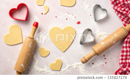 Heart-shaped dough pieces lie on a floured surface with a rolling pin and cutters Heart-shaped dough pieces lie on a floured surface with a rolling pin and cutters 135827278