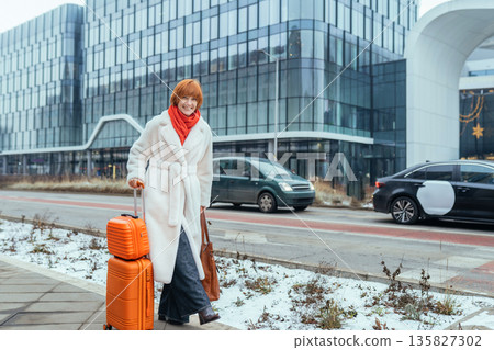 Full body middle aged woman smiling and pulling suitcase on urban street near modern office complex. City travel, relocation journey, positive emotion, solo female, winter travel Full body middle aged woman smiling and pulling suitcase on urban street near modern office complex. City travel, relocation journey, positive emotion, solo female, winter travel 135827302