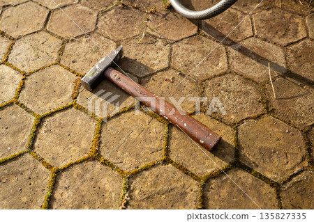 Old hammer with a wooden handle lying on hexagonal stone pavement. Tool for construction or repair work. Concept of home improvement and DIY 135827335