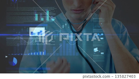 Male doctor in scrubs holding stethoscope earpieces to ears in lab, with floating data charts 135827403