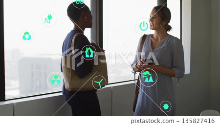 Two colleagues discussing sustainability ideas at office windows with smartphone and eco-icons Two colleagues discussing sustainability ideas at office windows with smartphone and eco-icons 135827416