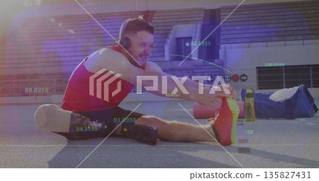 Mid-adult athlete stretching on stadium track, wearing red top with prosthetic leg and headphones 135827431